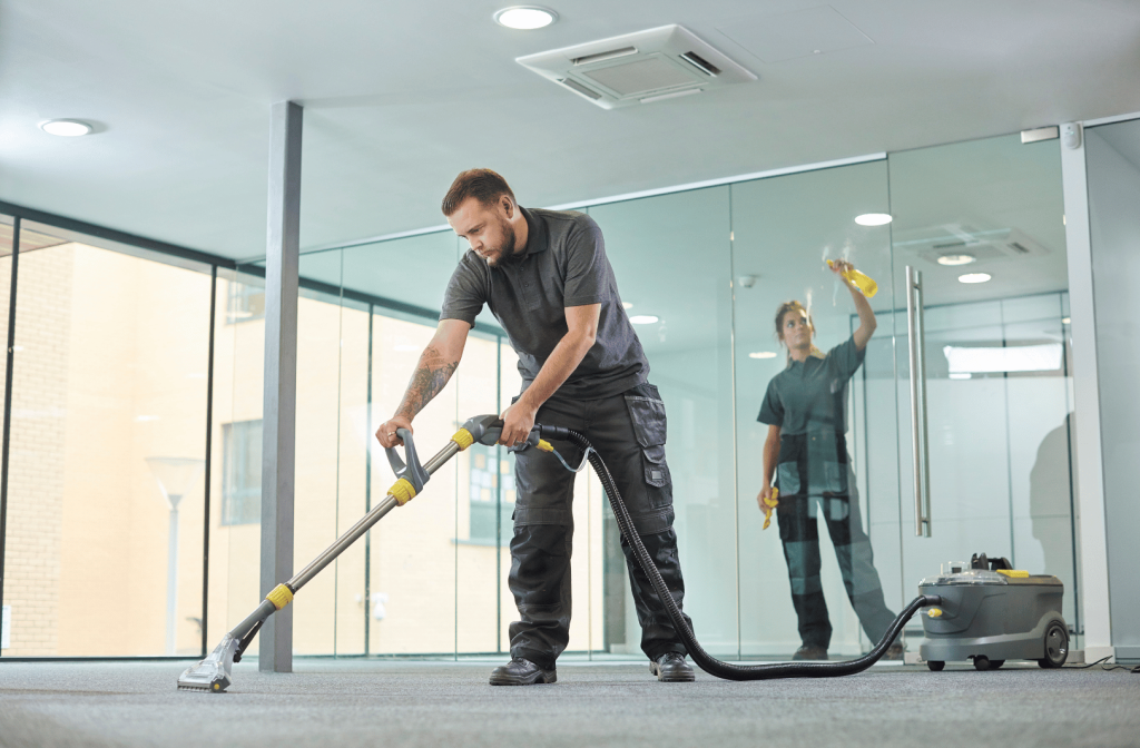 Two office cleaning staff vacuuming and disinfecting a workspace